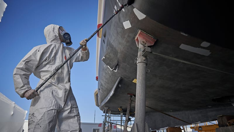 Technician in protective gear painting the hull of a superyacht during refit work at Pendennis Vilanova.