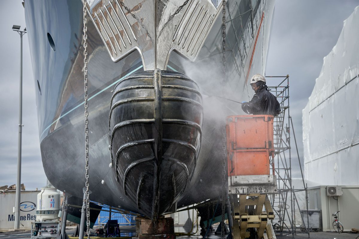 Shipyard technician pressure washing the bow of a superyacht at Pendennis Vilanova’s technical service centre.