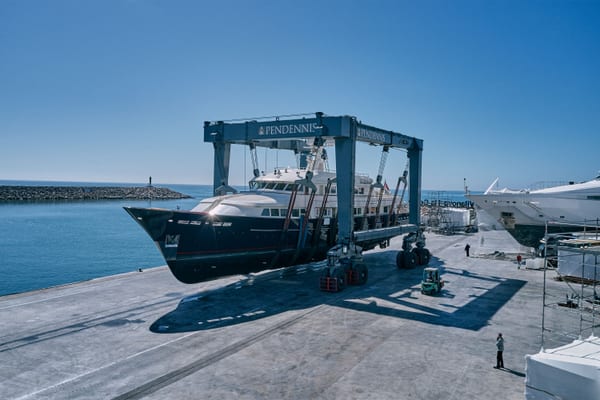 Superyacht suspended in Pendennis's 620-tonne travel hoist at Vilanova Technical Service Centre, with the marina in view.