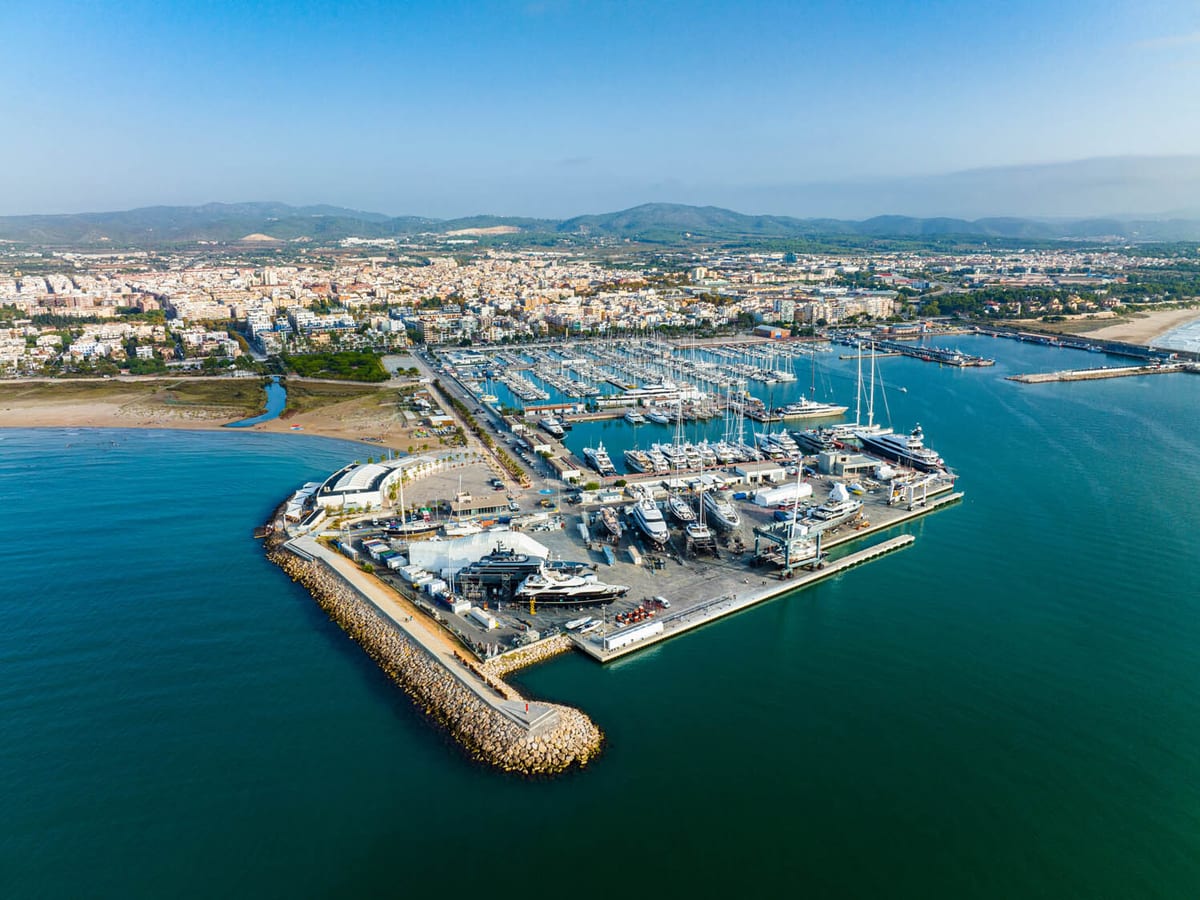 Panoramic aerial view of Pendennis Villanova's strategic Mediterranean location showing the expansive marina facilities, superyacht servicing area, and proximity to coastal town with mountain backdrop